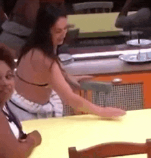 a woman in a bikini is sitting at a table in a kitchen .