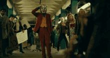 a man in a joker costume stands in a crowd holding a sign that says ps