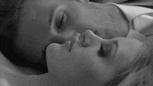 a black and white photo of a man and a woman laying next to each other on a bed .