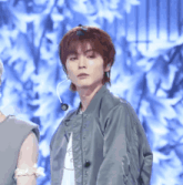 a young man wearing a bomber jacket and a microphone looks at the camera