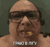 a bald man wearing glasses and a headset is eating a piece of food .