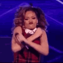 a woman in a plaid dress is crossing her arms and making a funny face .