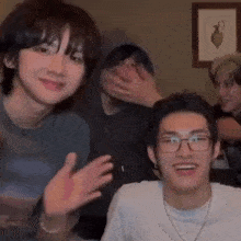 a group of young men are sitting in a living room . one of the men is wearing glasses .