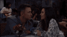a man and a woman are sitting at a table with a martini glass and a guitar player in the background .