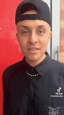 a man wearing a black hat and a black shirt is standing in front of a red door .