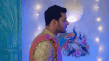 a man in a colorful dress is standing in front of a painting of a peacock .