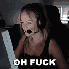 a woman wearing headphones and a microphone is sitting in front of a computer screen with the words oh fuck written on it .