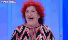 a woman with red hair is laughing in front of a blue background with the word viperissima on it .