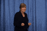 a woman is standing in front of a blue curtain and says and i don 't do any of it