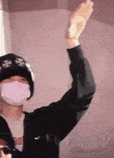 a man wearing a face mask and a hat is waving his hand .