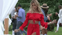 a woman in a red off the shoulder top and high slit skirt is dancing in a crowd of people .