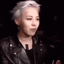 a young man with white hair is wearing a black leather jacket and a black shirt .