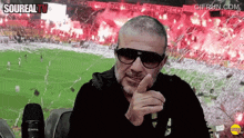 a man wearing sunglasses is pointing at the camera in front of a soccer field with the words soureal tv written above him