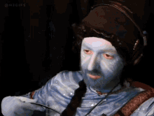 a man with blue paint on his face is wearing headphones and holding a spoon .
