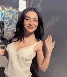 a woman with long black hair is wearing a white tank top and smiling