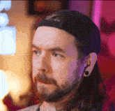 a man with long hair and a beard wearing a hat and ear plugs .
