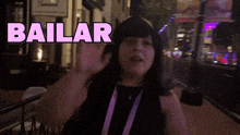 a woman wearing a black hat and a purple lanyard says bailar