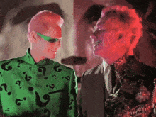 a man and a woman are standing next to each other and the woman is wearing a green shirt with question marks on it