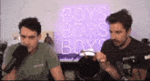 two men are sitting in front of a purple sign that says boys boys boys