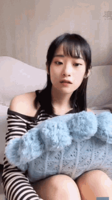 a woman is sitting on a bed holding a blue pillow .