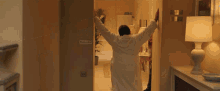 a man in a bathrobe stands in a hallway with his arms outstretched in front of a clapper board