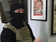 a man wearing a black mask stands in front of a framed life magazine cover