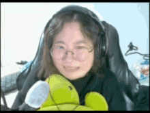a woman wearing headphones and glasses is holding a stuffed turtle .