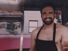 a shirtless man with a beard is wearing an apron and smiling