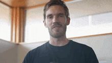 a man with a beard and mustache is standing in front of a window and looking at the camera .