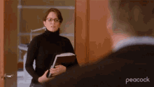 a woman in a black turtleneck is holding a binder and talking to a man in a peacock advertisement