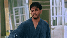 a man in a blue robe is standing in front of a door and looking at the camera .