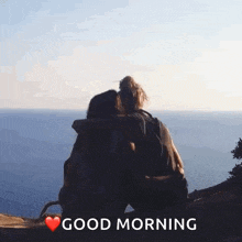 a couple of people hugging each other while sitting on a hill overlooking the ocean .