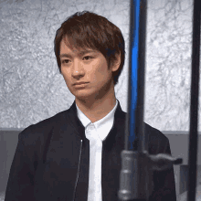 a man wearing a black jacket and a white shirt stands in front of a blue pole