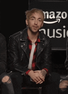 a man in a black leather jacket sits in front of an amazon music logo