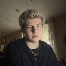 a young man wearing a black shirt and a cross necklace looks at the camera