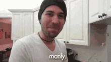 a man wearing a beanie and a white shirt is standing in a kitchen and says manly .
