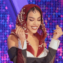 a woman wearing a red scarf on her head is smiling and making a heart shape with her hands .