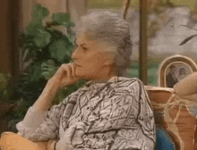 an elderly woman is sitting on a couch with her hand on her chin and looking at the camera .