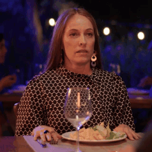a woman sitting at a table with a plate of food and a wine glass
