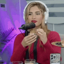 a woman wearing headphones is sitting in front of a microphone eating a cookie .