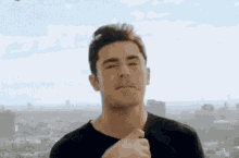a man in a black shirt is looking at the camera with a city in the background .