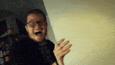 a man with glasses and a beard is laughing with his mouth open