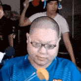 a bald man wearing glasses and a blue shirt is sitting in front of a crowd .