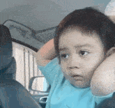a young boy is sitting in the back seat of a car with his hands on his head .