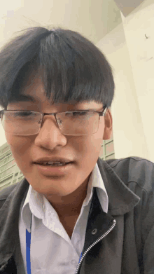 a young man wearing glasses and a black jacket is looking at the camera
