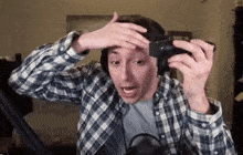 a man wearing headphones and a plaid shirt is holding a camera