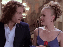 a man in a suit and a woman in a pearl necklace are looking at each other