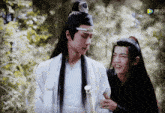 a man in a white robe stands next to a man in a black robe with chinese writing on the screen