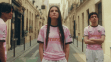 a woman wearing a pink shirt that says orange stands next to two men