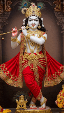 a statue of krishna playing a flute in a red and gold outfit